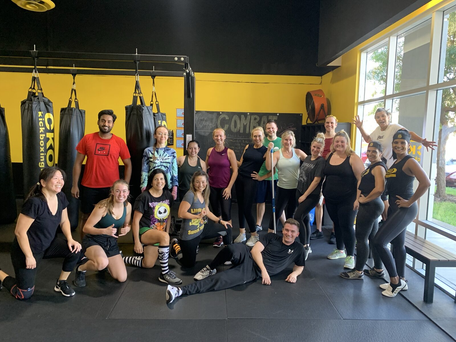 Adult kickboxing class group photo, smiling, in a gym with heavy bags
